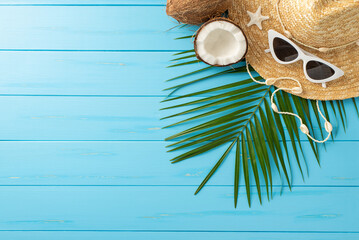 Top view of beach accessories: straw hat, sunglasses, coconut, and seashells on a vibrant turquoise...