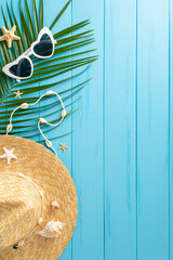 Vertical arrangement of beach essentials for summer vacation showcasing a straw hat, sunglasses,...