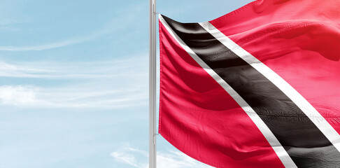 Trinidad and Tobago national flag with mast at light blue sky.