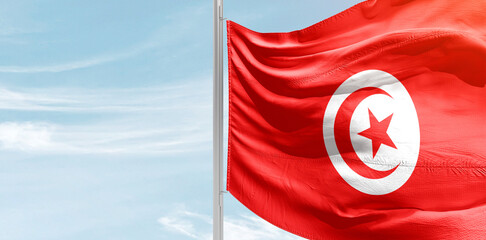 Tunisia national flag with mast at light blue sky.