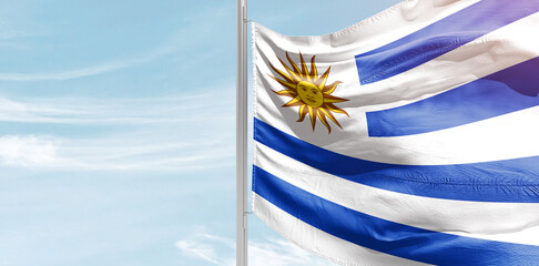 Uruguay national flag with mast at light blue sky.