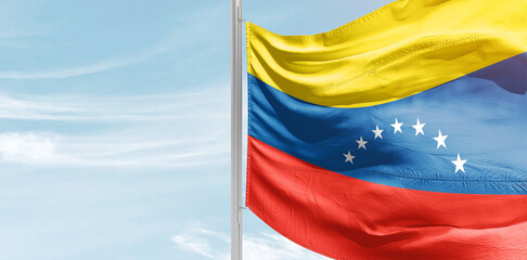 Venezuela national flag with mast at light blue sky.