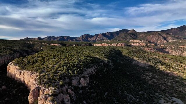 Aerial immersive establishment shot of steep red cliffs, covered in pinion pines in rural Colorado.  The setting sun casts shadows creating beautiful contrast.  This particular area is a hot spot for 