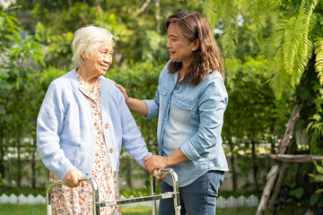 Doctor caregiver help and care Asian senior woman patient walk with walker in park at hospital.