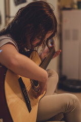 Close up of a teenage girl learning to playing acoustic guitar at home. Young girl playing music on...