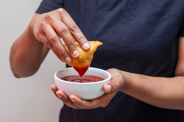 a lady dipping Samosa on tomato sauce. Indian street food. 