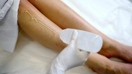 Body cream or anti-cellulite scrub, smear of gel on female leg. A professional cosmetologist applies gel to a client's leg before a laser hair removal procedure in a salon, close-up.