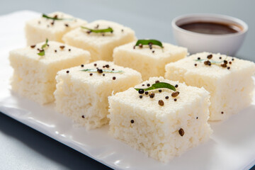 White dhokla plated in a white plate on a grey background with negative space to write copy.