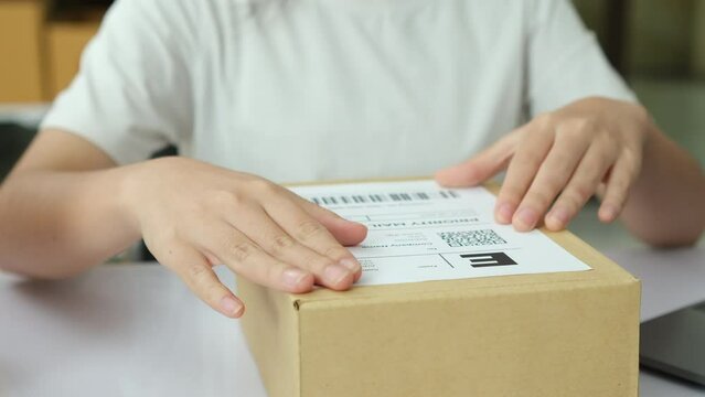 Close-up Shot of Professional Warehouse Worker Checks and Seales Cardboard Box Ready for Shipment. In the Background Rows of Shelves with Cardboard Boxes with Ready Orders.