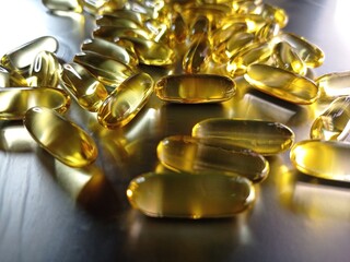 A pile of omega-3 fish oil capsules on a silver background. Close-up of large golden translucent...