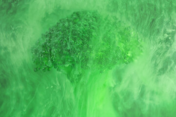 Fresh broccoli in cloud of green color paint in water. Artistic nutrition concept. Science of food...