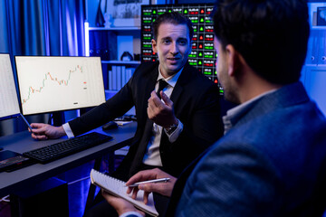 Fototapeta na wymiar Two stock exchange traders discussing on dynamic investment graph, trending of high profit in currency stock. Showing financial benefit data on monitor screen in neon light at workplace. Sellable.