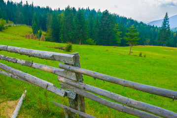 closeup wooden fence on green mountain pasture, summer mountain village scene