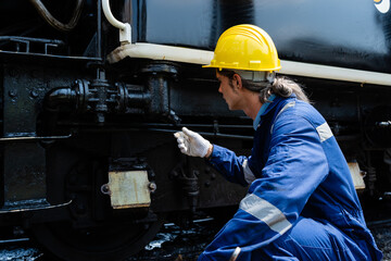 A man in a yellow helmet is working on a train. He is wearing a blue jumpsuit and white gloves