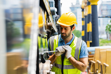 A man in a yellow and green vest is working on a machine. He is wearing a hard hat and gloves