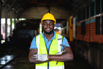 A man in a yellow vest and a hard hat is standing in a train station. He is smiling and looking at...