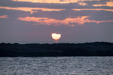 Alba sul mare con cielo nuvoloso, sole, e riflesso del sole sull'acqua.