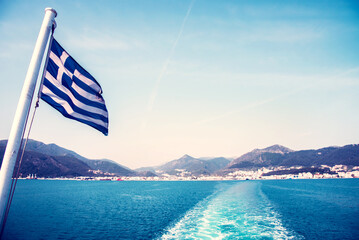 National flag of Greece on a ferry on the background of Greek island landscapes and the trace of...