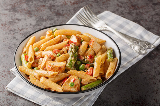 Creamy chipotle chicken penne pasta with asparagus, peppers, green peas, onion and garlic close-up in a bowl on the table. horizontal