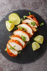 Delicious spicy chipotle chicken breast served with lime and cilantro close-up on a slate plate on the table. Vertical top view from above