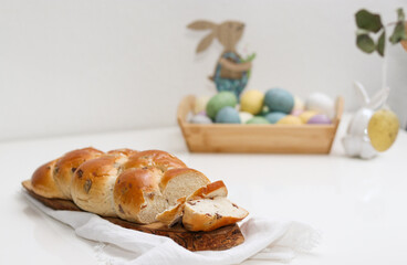 Cutted easter loaf bread on wooden plate on white table, blurry background with easter decoration