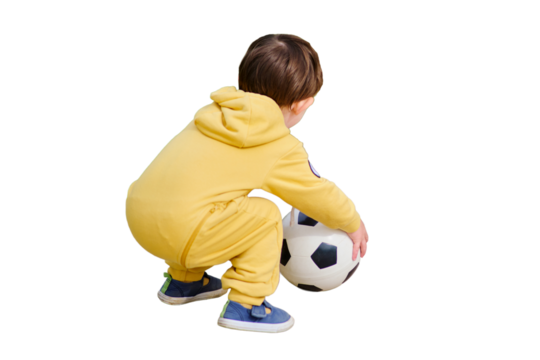 A toddler baby is kicking a football on the green grass in the park, isolated on white background. Kid aged two years (two-year-old boy)