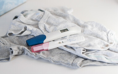 Fototapeta na wymiar Close up of two positive pregnancy tests on baby clothes