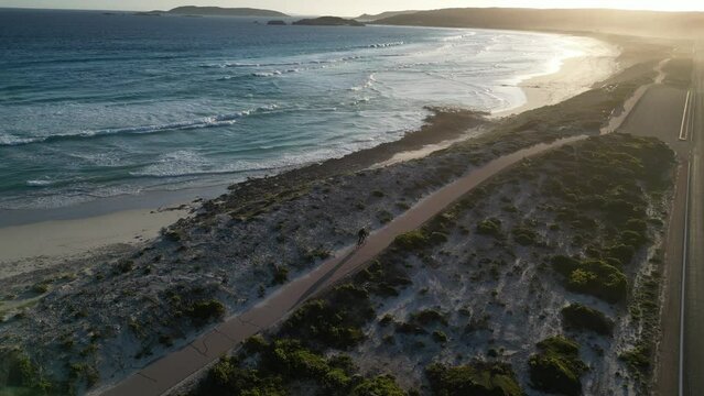 Cyclist pedaling on cycle path along Salmon Beach at sunset, Esperance in Western Australia. Aerial drone view and slow-motion