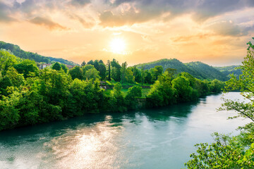 beautiful landscape of spring or summer sunset river with blue water and green hills on sides and...