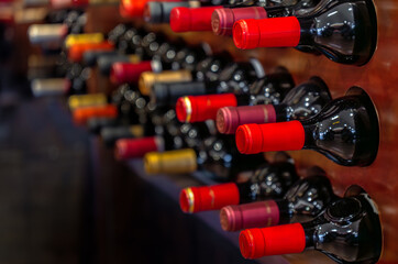 Close-up detail of black red wine bottles with red labels aligned and stacked horizontally on wooden shelves and bottle racks in a luxury collectible wine store