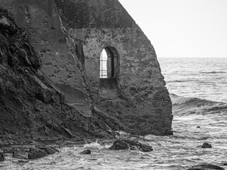 Remains of an Ancient Wall with a Window and the Waves of the Sea Rushing in