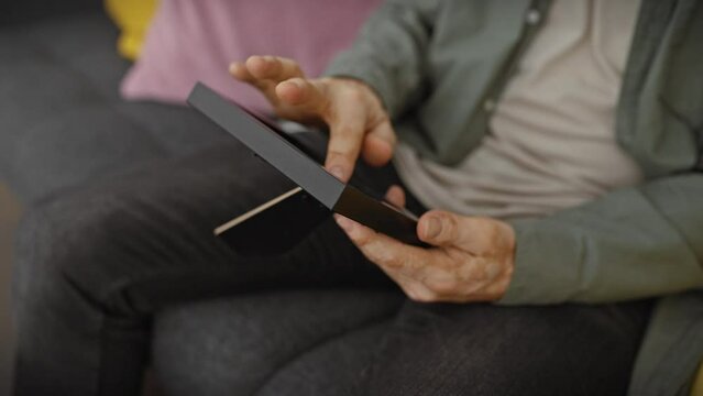 Hispanic man holding smartphone at home on couch, technology and lifestyle concept