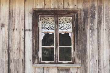 Wooden rustic window in cottage house. Lace curtains glass window home. Rusty architecture. Podlasie region in Poland vintage wall. Wood home wall facade. Village farm building.