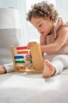 little girl with curly hair playing sitting on the carpet in her room with a wooden toy made of beads, numbers and colors. montessori material concept development and learning in the childhood stage.