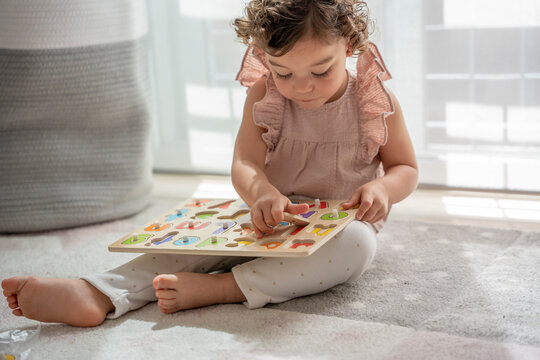 horizontal image of a little girl with curly hair playing sitting on the carpet in her room with a wooden alphabet, Montessori material. concept development and learning in the childhood stage.