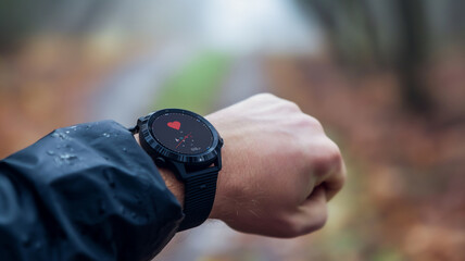 Smartwatch on a wrist displaying heart rate monitor, outdoors on a rainy day.