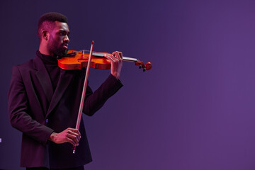 Professional violinist in black suit performing on a vibrant purple background with artistic...