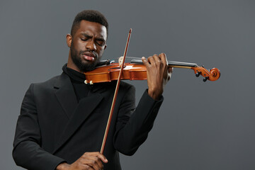 Elegant African American Man in Black Suit Playing Violin on Gray Background, Musical Performance...