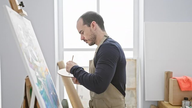 Bald bearded man painting on canvas in a bright studio setting, reflecting art, creativity, and concentration.