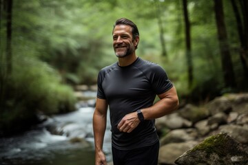 Portrait of a content man in his 40s wearing a moisture-wicking running shirt while standing against tranquil forest stream