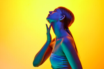 Side view photo of young sensual woman touching her neck in neon light against yellow gradient...