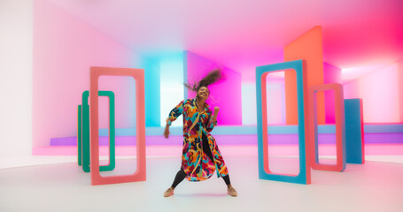 Beautiful Smiling Black Woman Dancing Energetically in a Colorful Abstract Neon Lit Studio. Talented Stylish Female Dancer Performing a Modern Choreography, Having Fun, Making Moves, Practicing. - obrazy, fototapety, plakaty