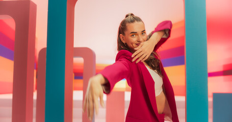 Medium Shot of an Attractive Woman in a Fashionable Outfit Moving her Hands Gracefully While Dancing and Looking at Camera. Female Dancer Performing Choreography in a Spacious Colorful Studio.