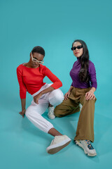 Two fashion models with sunglasses posing with attitude on a blue studio background. High quality photo