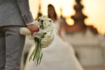 In the wedding ceremony,the groom holding white bouquet waiting for his bride. Both of them stand...