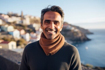 Portrait of a cheerful indian man in his 50s wearing a classic turtleneck sweater isolated in picturesque seaside village