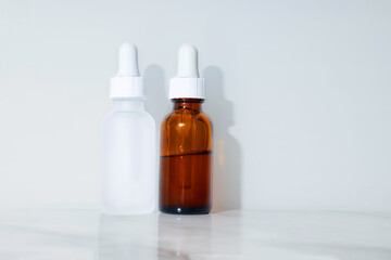An exhibits of two small transparent and brown bottles of beauty serum with  a white background