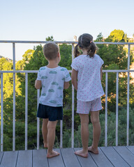 Cute children boy and girl are standing on the balcony and looking into the distance. Brother and...
