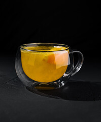 Glass mug of warm citrus tea on dark background