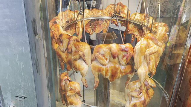 Golden roasted chickens spin slowly in a rotisserie, their crispy skins glistening, classic and irresistible street food staple beckoning passersby with its mouthwatering aroma. Chicken grill